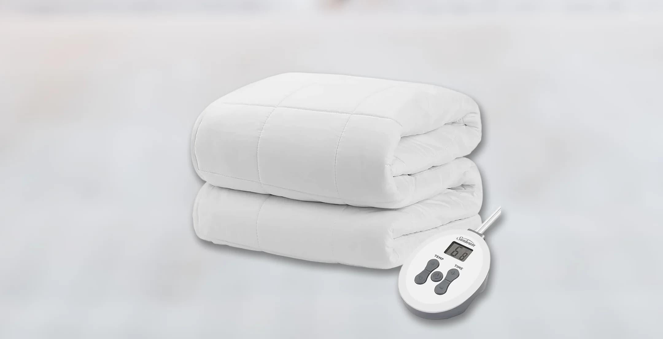 A folded white electric blanket with a digital controller displaying temperature settings. The background is smooth and softly blurred, conveying a sense of comfort.